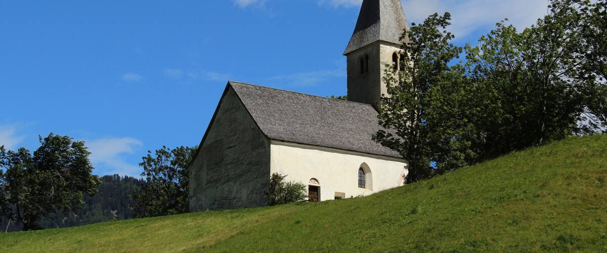 A church with a tall steeple on a grassy hill under a blue sky.