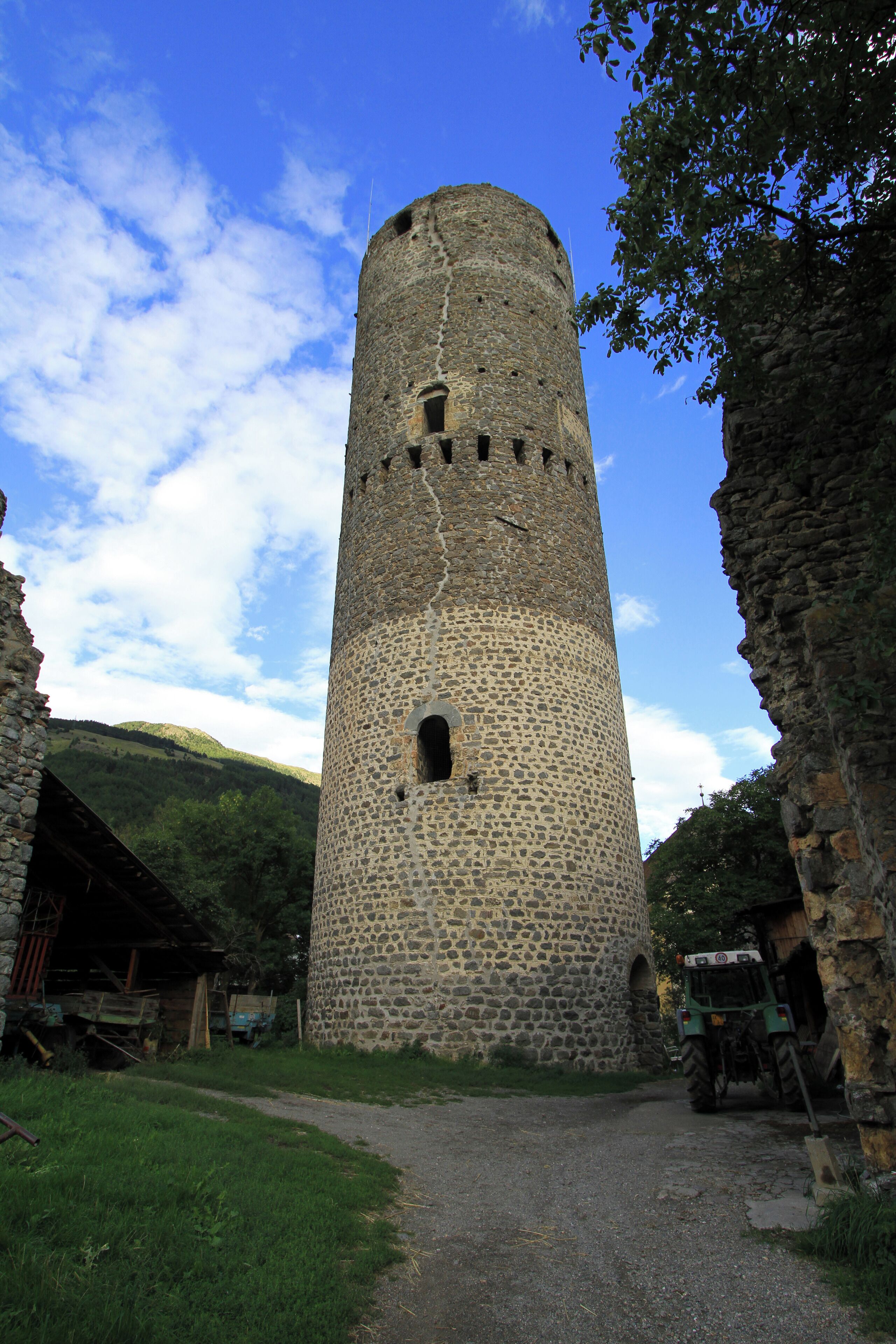 A stone tower with a narrow entrance, surrounded by greenery and a clear sky.