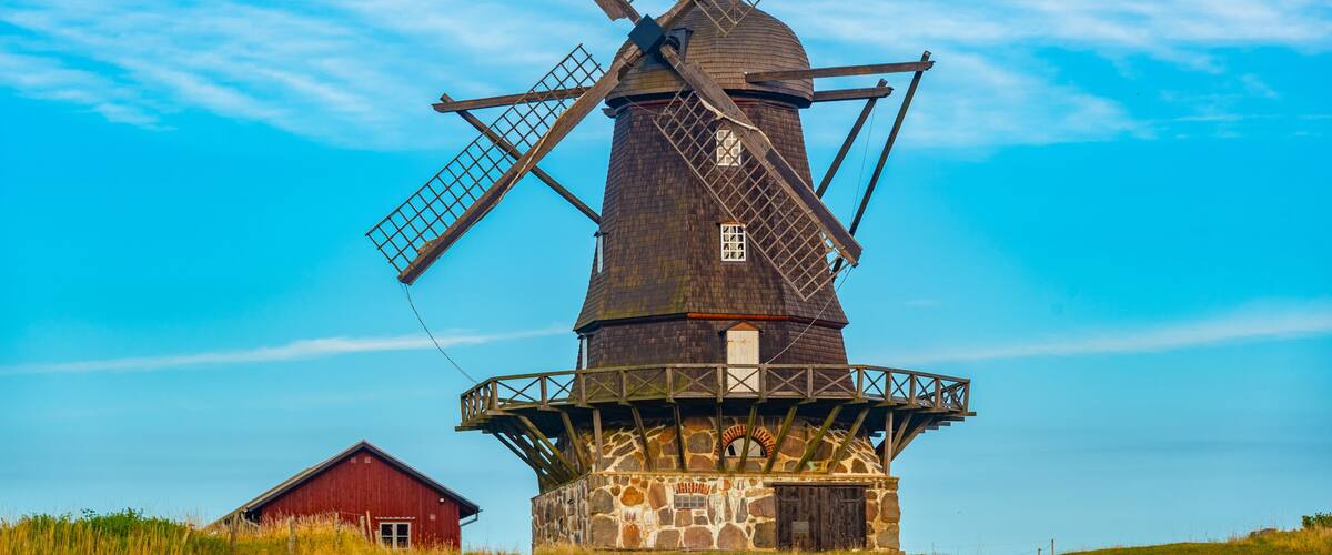 A traditional windmill with wooden blades and a stone base, set against a clear blue sky.