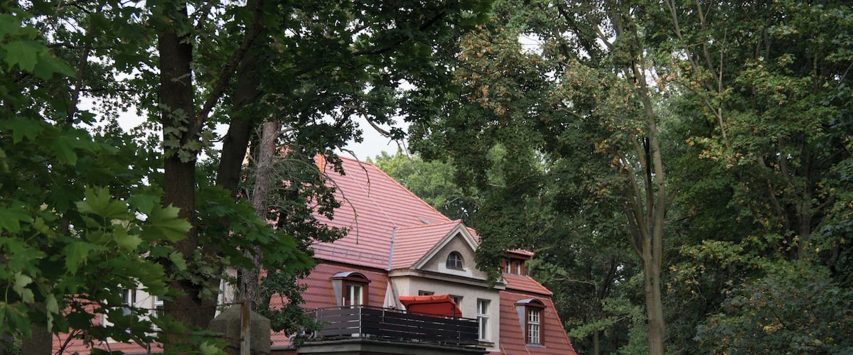 A two-story house with a red roof, surrounded by trees and greenery.