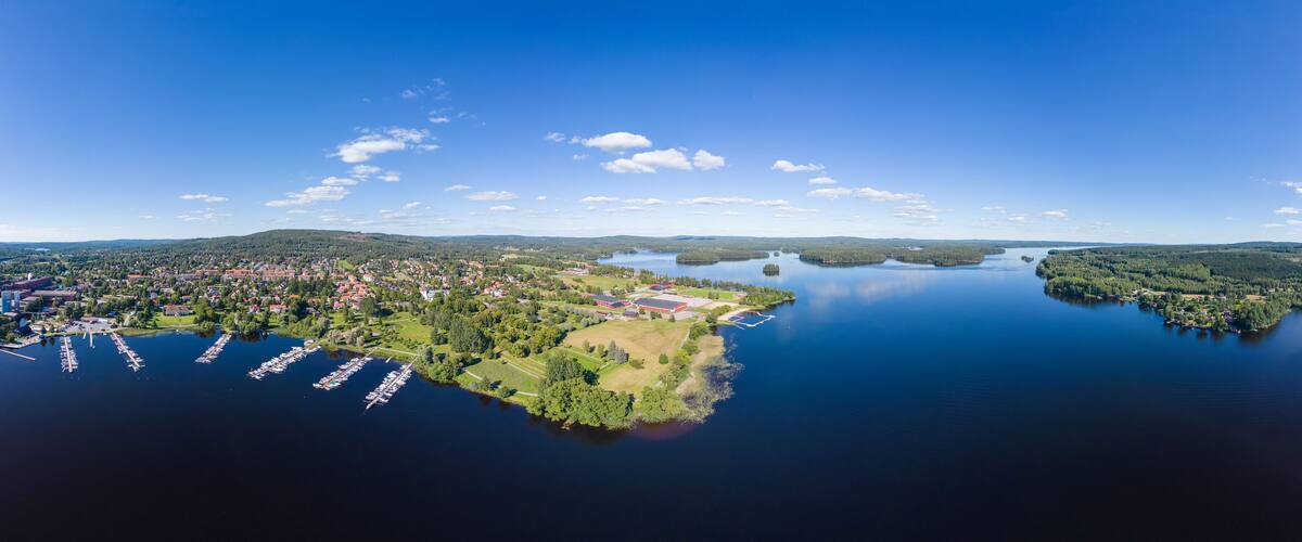 An aerial view of a lakeside town with a marina, green hills, and a clear blue sky.