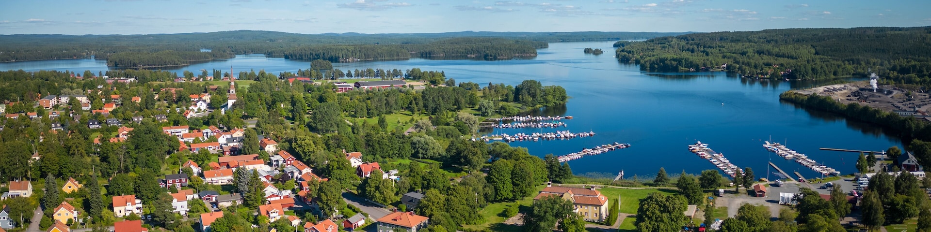 Un pueblo a orillas del lago con casas de techo rojo, un puerto deportivo y un faro.