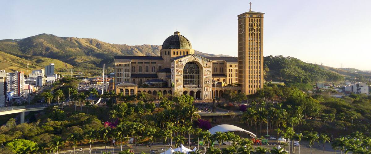 A large church with a dome and a tall tower, surrounded by palm trees and mountains in the background.