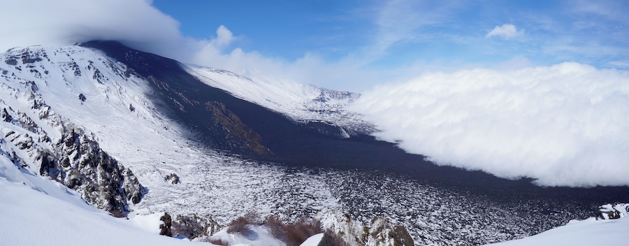 Una montaña nevada con un valle y nubes.