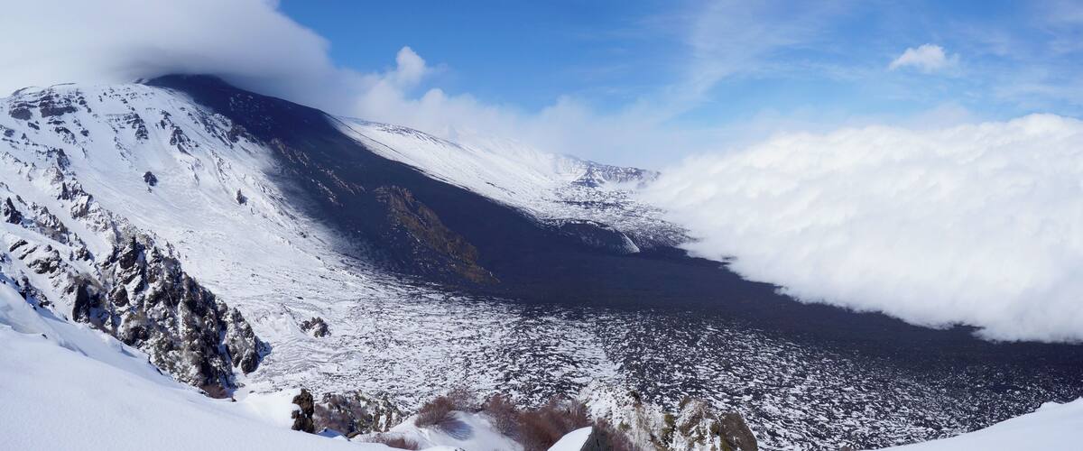 A snow-covered mountain with a valley and clouds.
