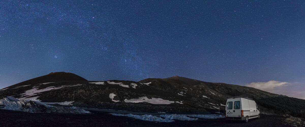 A white van parked in a snowy landscape with mountains under a starry night sky.