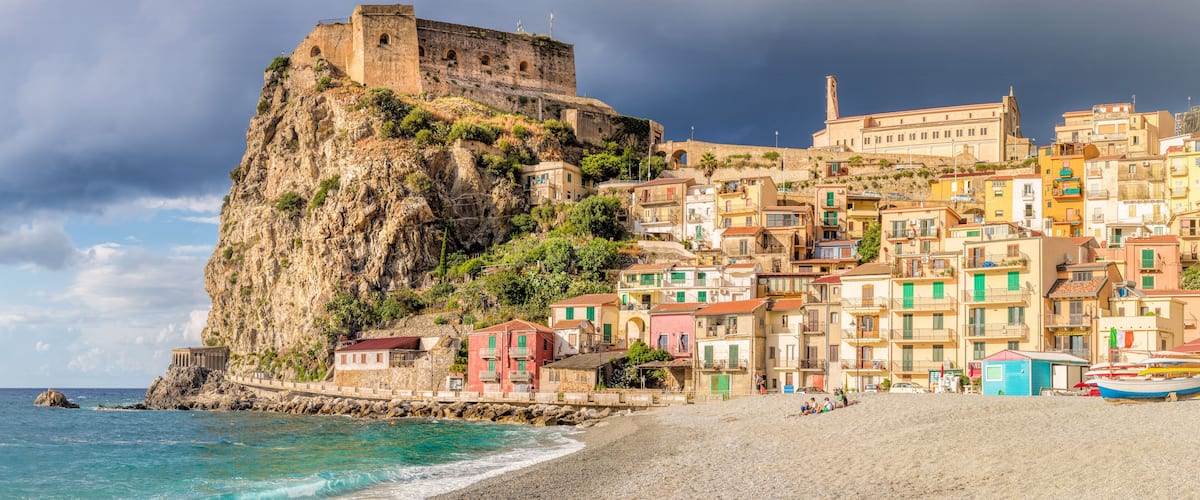 A coastal town with colorful buildings, a prominent cliff, and a historic fort.