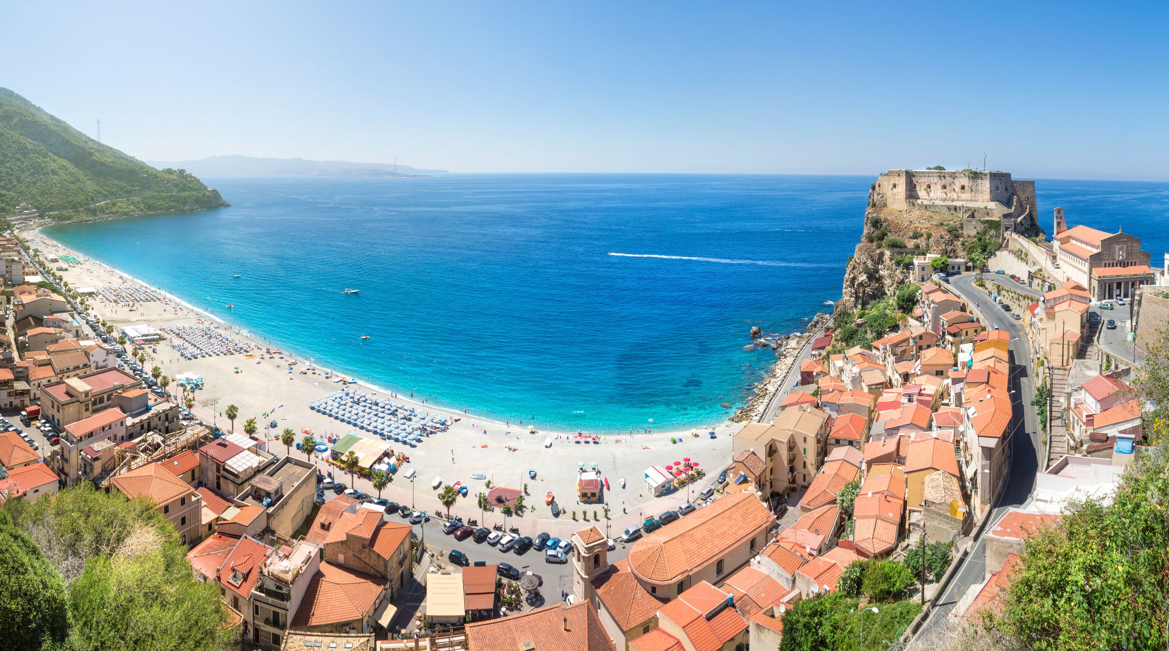 A coastal town with a beach, a fort, and terracotta-roofed buildings.