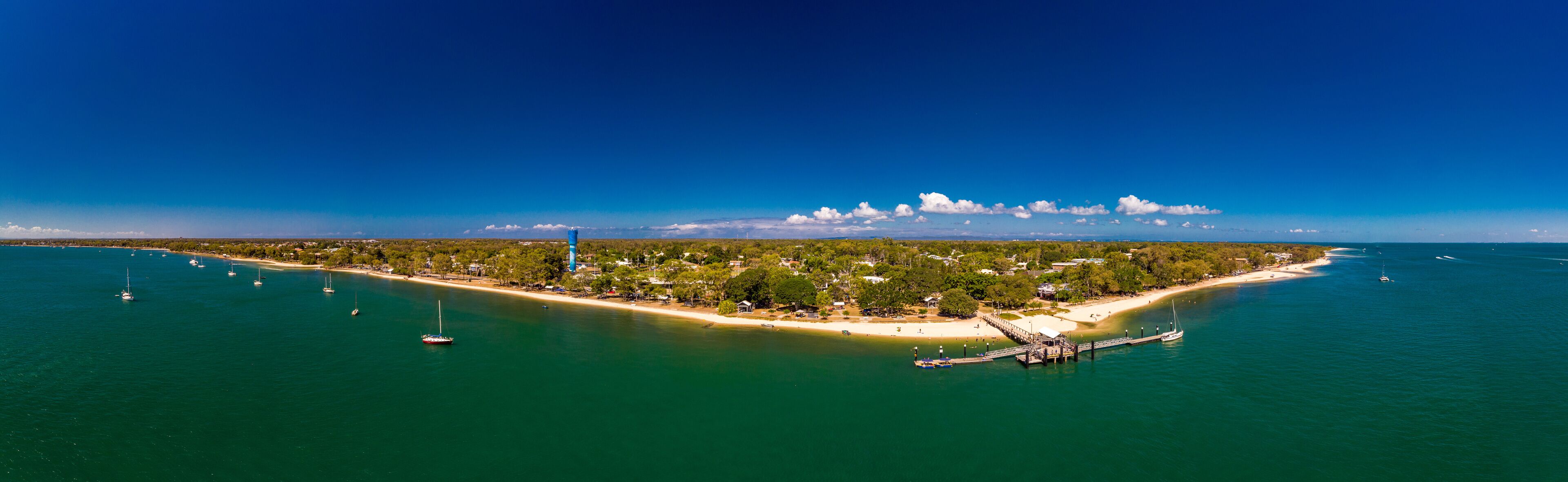 An aerial view of a coastal island with a lighthouse, sandy beaches, and clear blue waters.