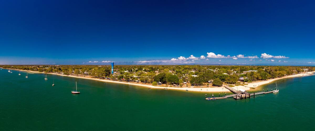 An aerial view of a coastal island with a lighthouse, sandy beaches, and clear blue waters.