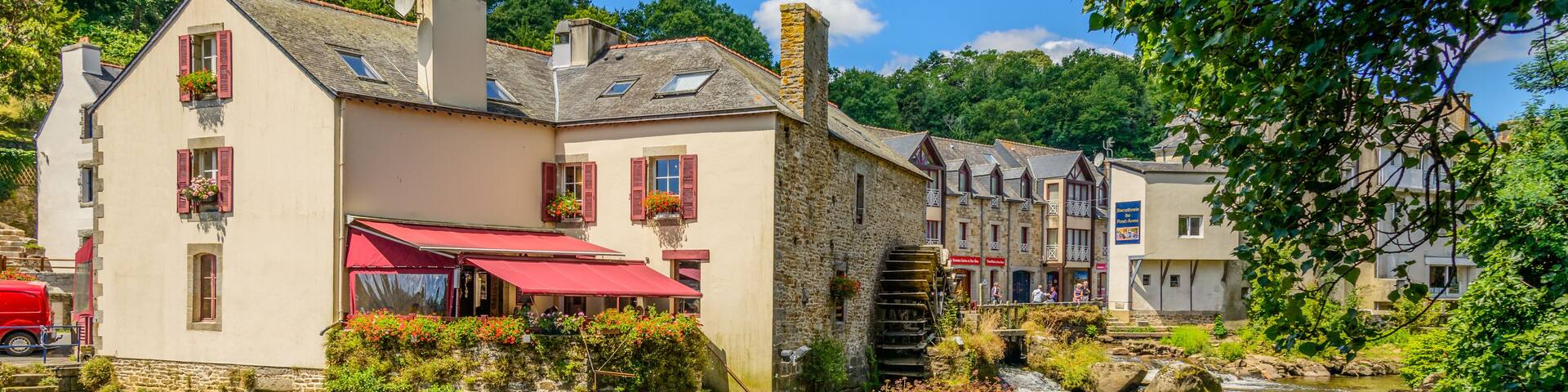 A river flowing through a village with stone buildings and a red-roofed café.