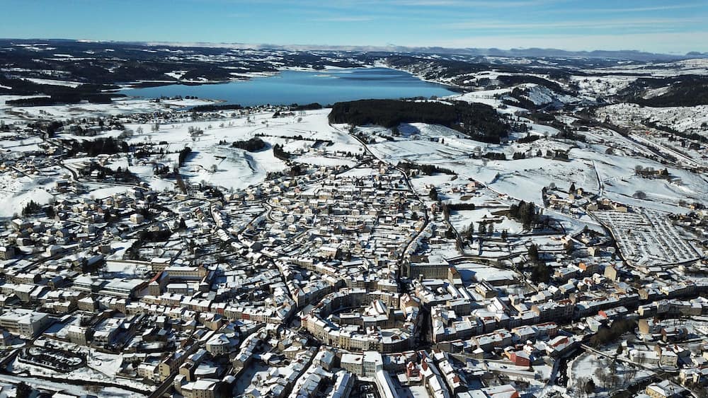 Une ville enneigée, avec un lac et des montagnes en arrière-plan.