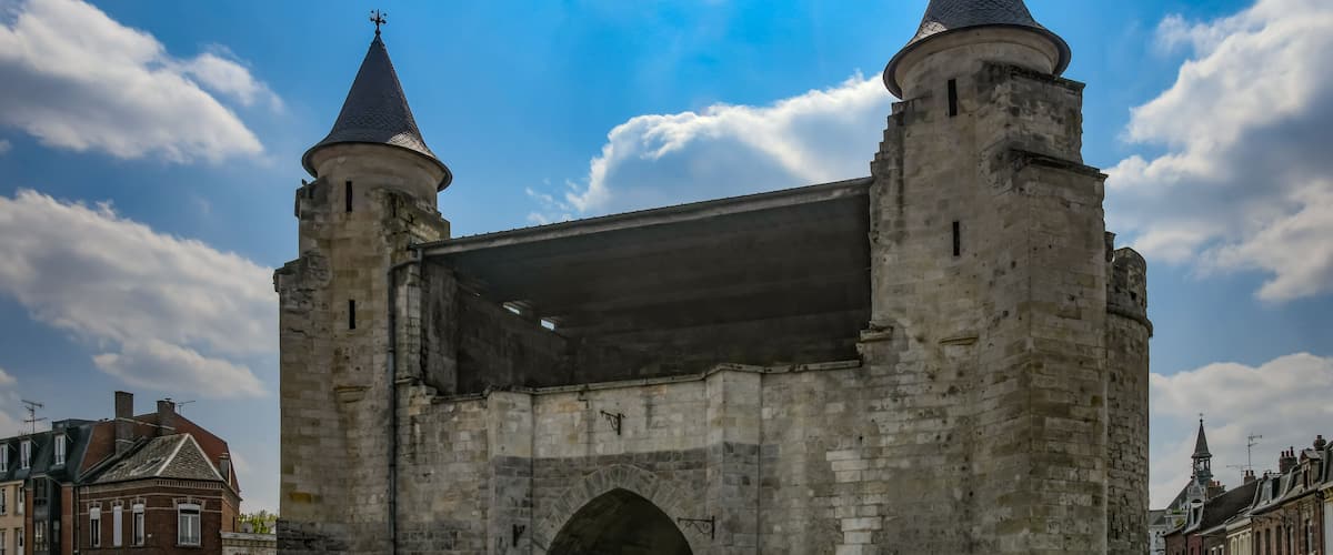 A stone archway with two towers, surrounded by a street and buildings.