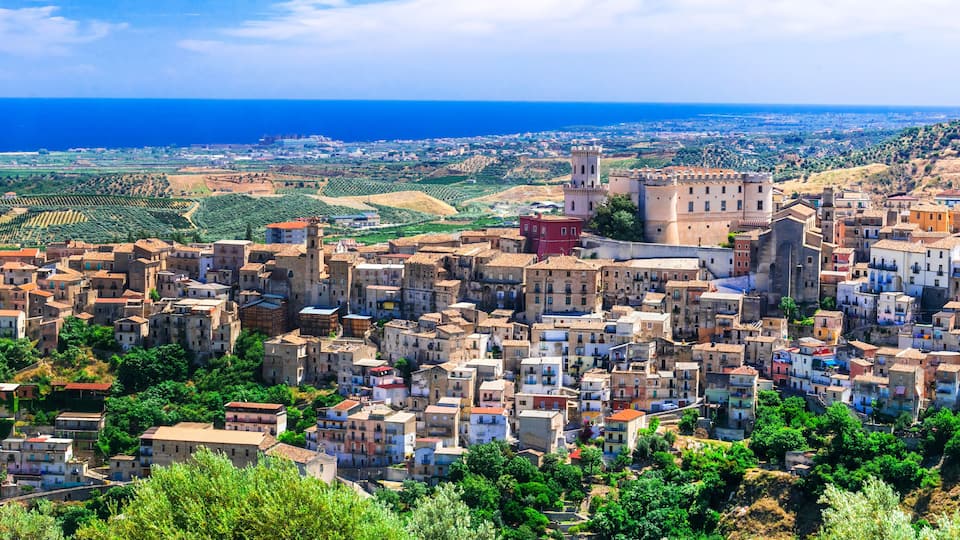 A coastal town with historic architecture, terraced vineyards, and a prominent castle overlooking the sea.