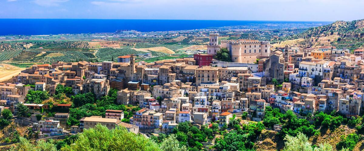 A coastal town with historic architecture, terraced vineyards, and a prominent castle overlooking the sea.