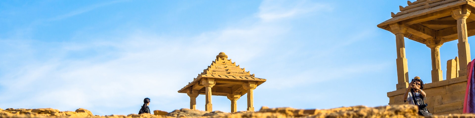 A rocky landscape with two stone structures, one with a pointed roof and another with a rounded roof, under a clear blue sky.