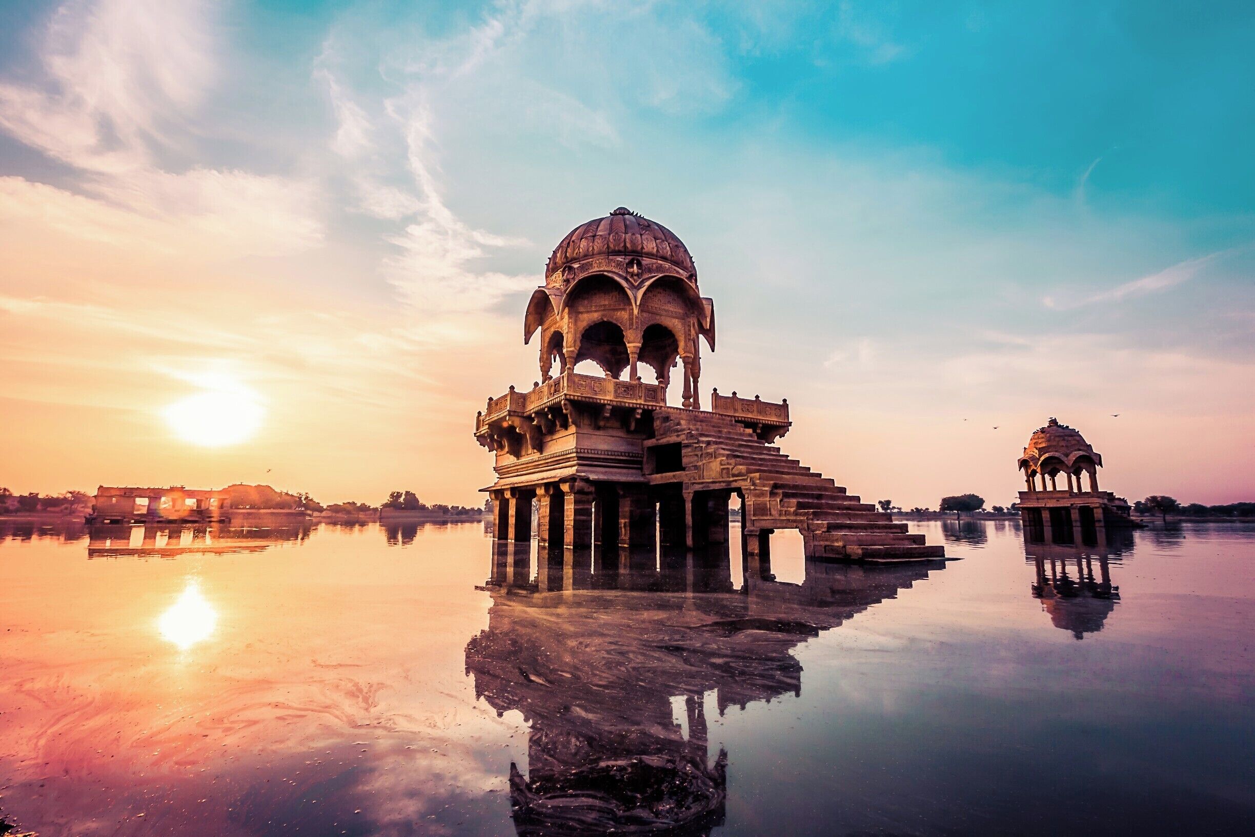 A reflection of a historical structure with a dome and arches in a calm body of water during sunset.