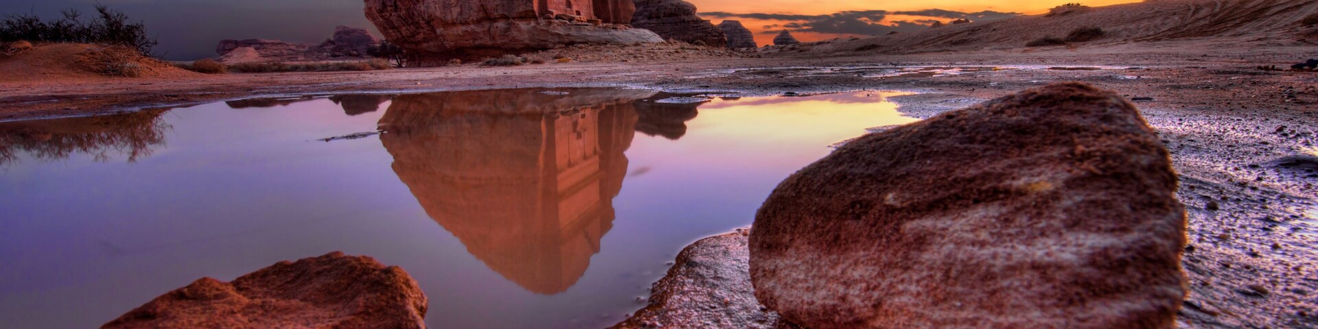 Formação rochosa refletida em águas rasas, com o céu ao pôr do sol como pano de fundo.
