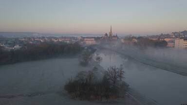 A river with a bridge, a church with a tall spire, and a town in the background.
