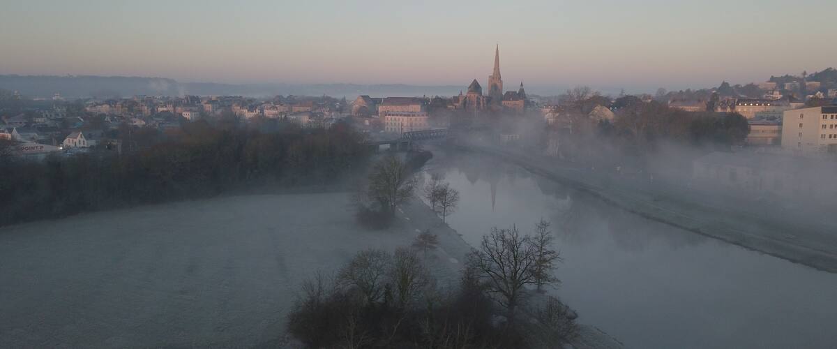 A river with a bridge, a church with a tall spire, and a town in the background.