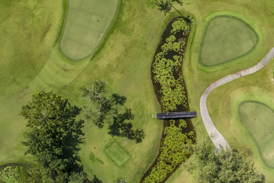 Eine Vogelperspektive eines Golfplatzes mit einer Brücke, Wasserhindernissen und Bäumen.