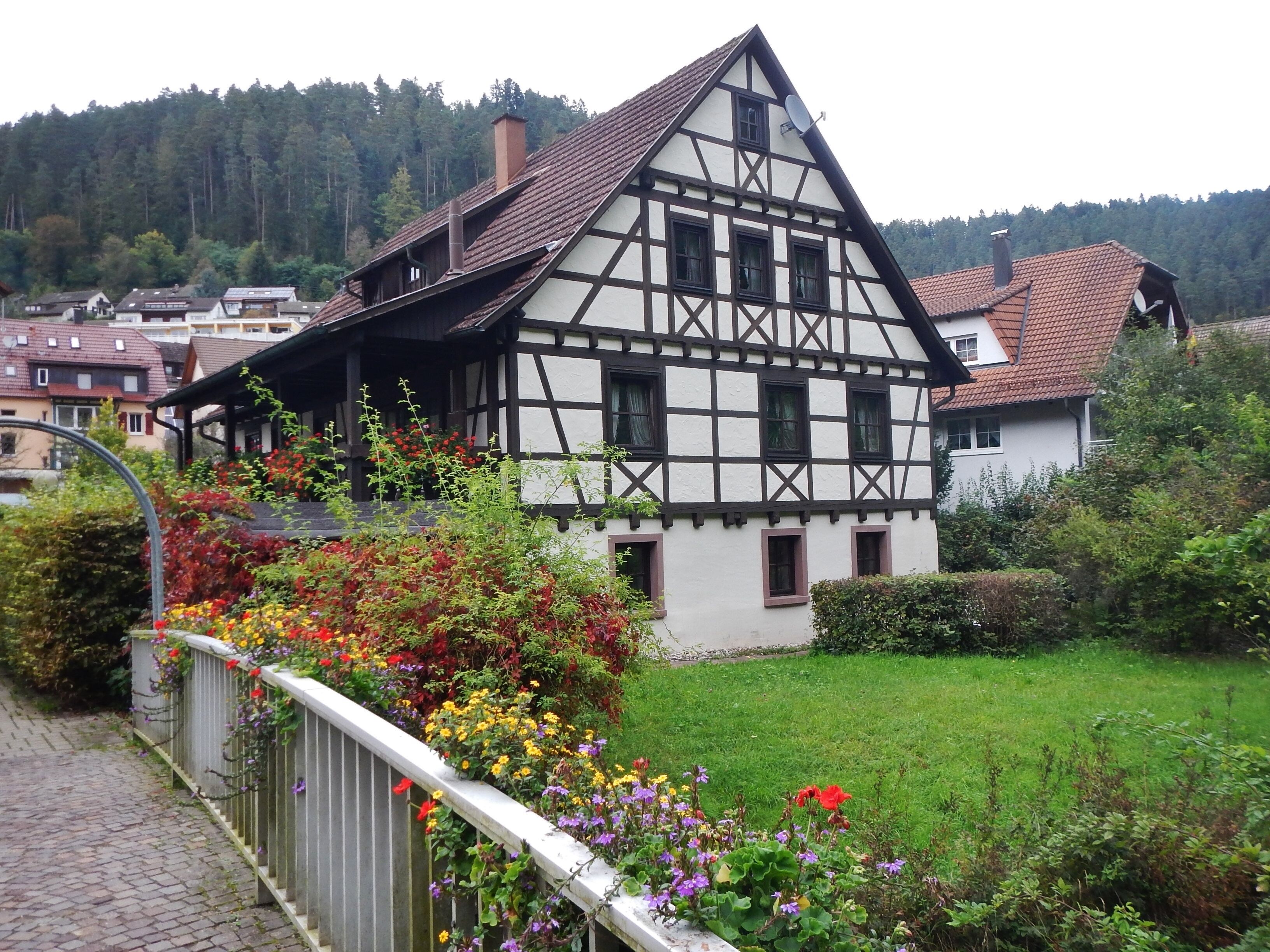 A traditional half-timbered house with a sloped roof, surrounded by a garden with colorful flowers and a cobblestone path.