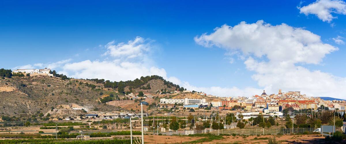 A hill with a building on top, a town in the valley below, and a clear blue sky.