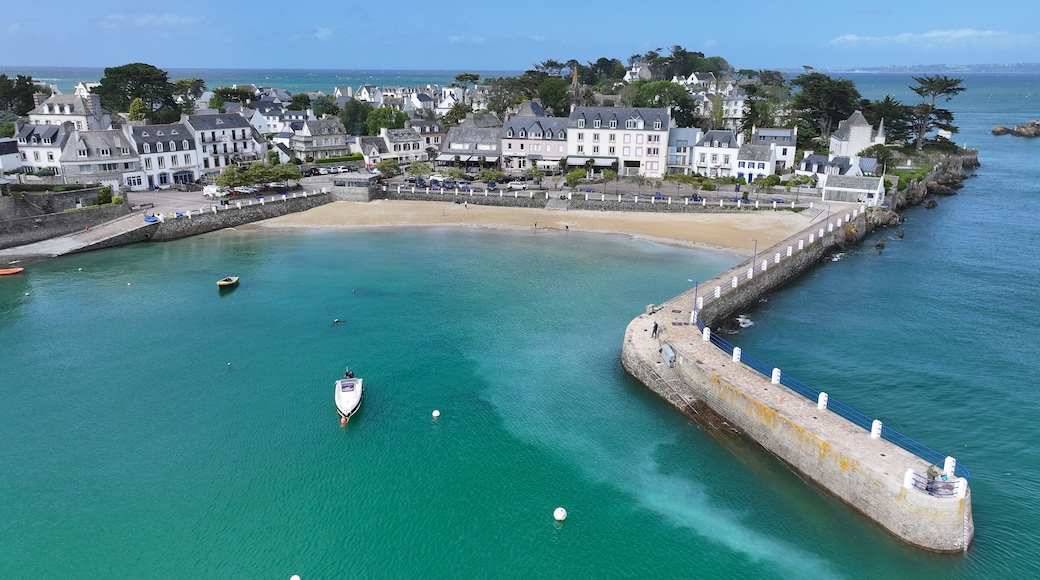 Aerial view of the picturesque harbor of Locquirec featuring a stone pier, sandy beach, and traditional coastal houses along the turquoise sea, Locquirec, Brittany, France.