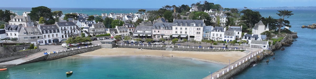 A coastal town with a clear harbor, a sandy beach, and a stone breakwater.