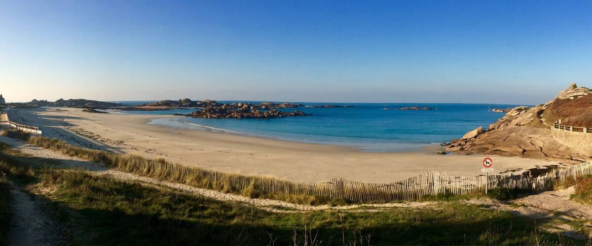 A beach with clear blue water, sandy shore, and rocky outcrops.