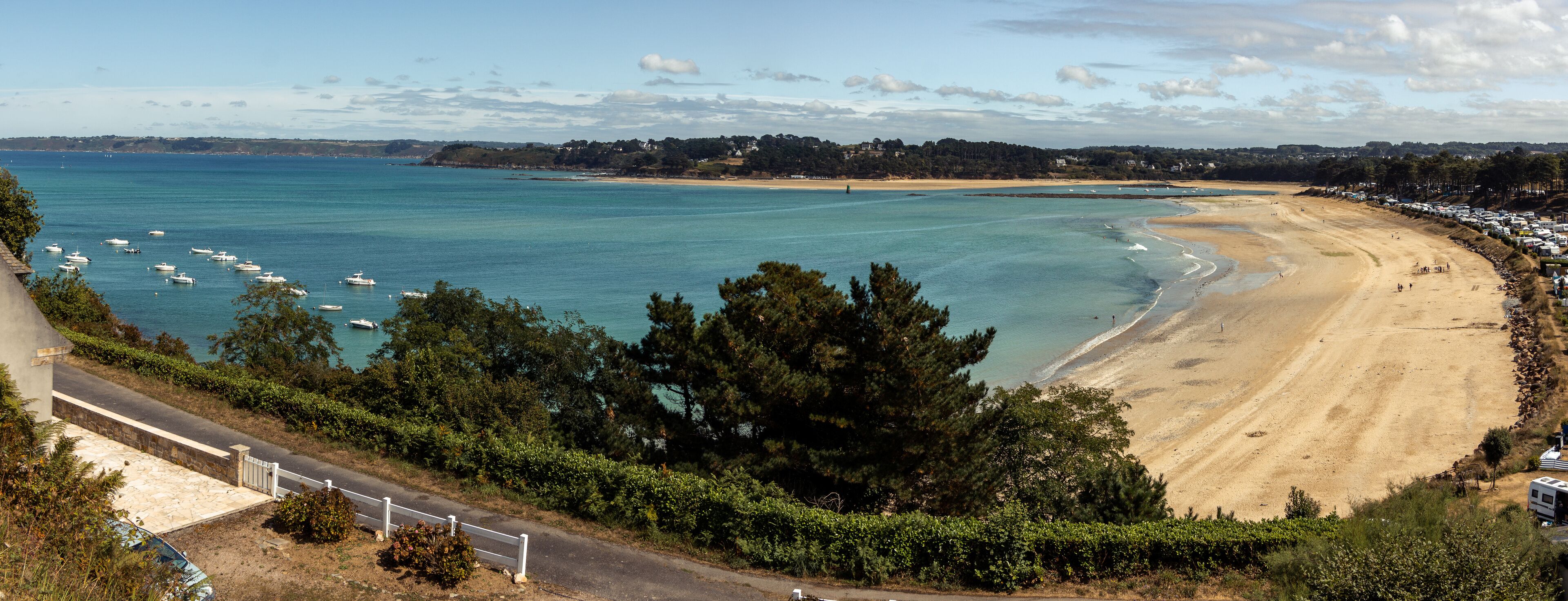A coastal beach with clear turquoise waters, a sandy shore, and a line of trees in the foreground.