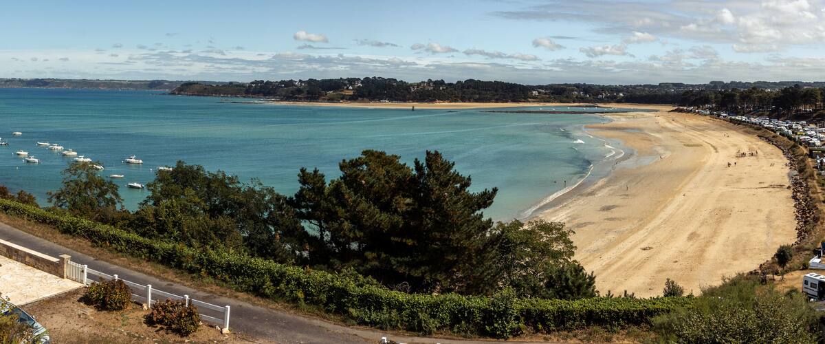 A coastal beach with clear turquoise waters, a sandy shore, and a line of trees in the foreground.