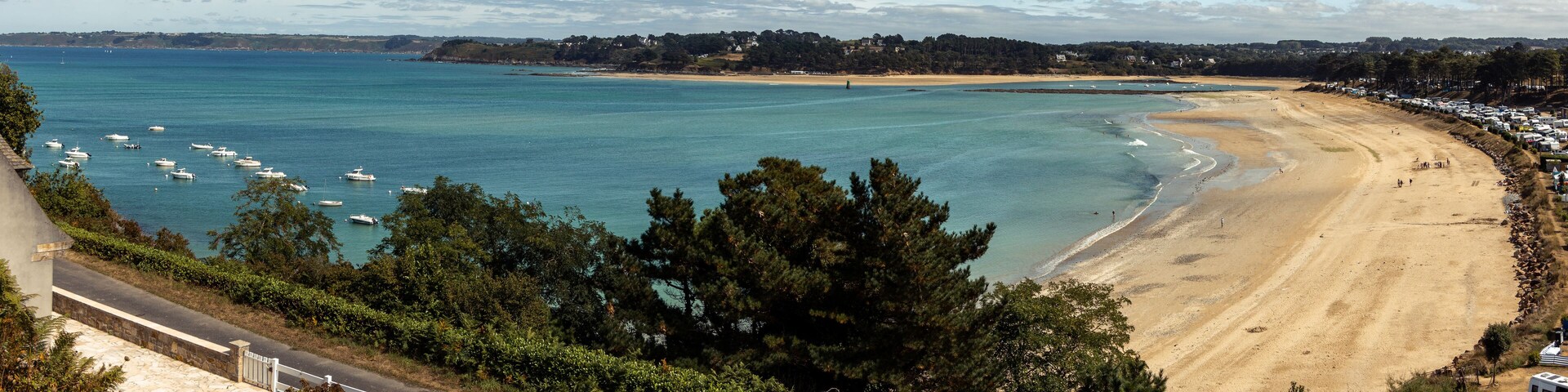 A coastal beach with clear turquoise waters, a sandy shore, and a line of trees in the foreground.