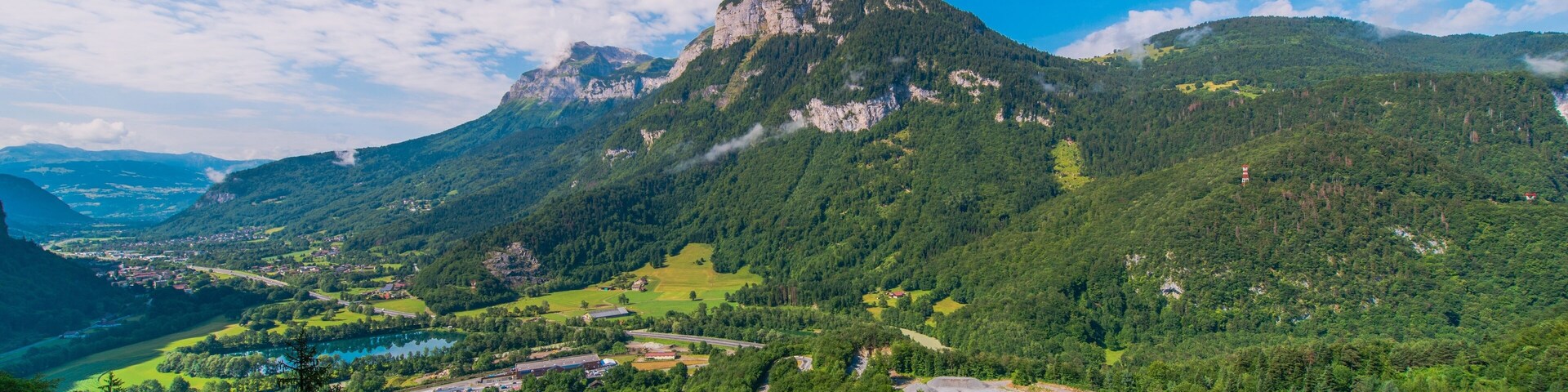 Un paisaje montañoso con un pico destacado, un valle con un pueblo pequeño y un río.