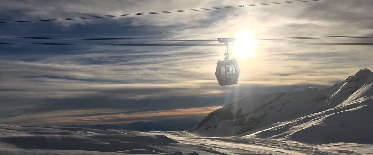 A cable car ascending a snowy mountain with a sunlit sky.