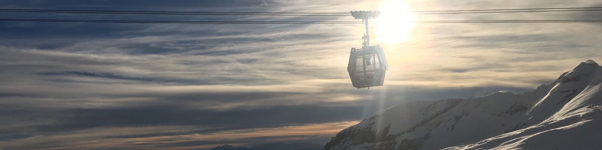 A cable car ascending a snowy mountain with a sunlit sky.