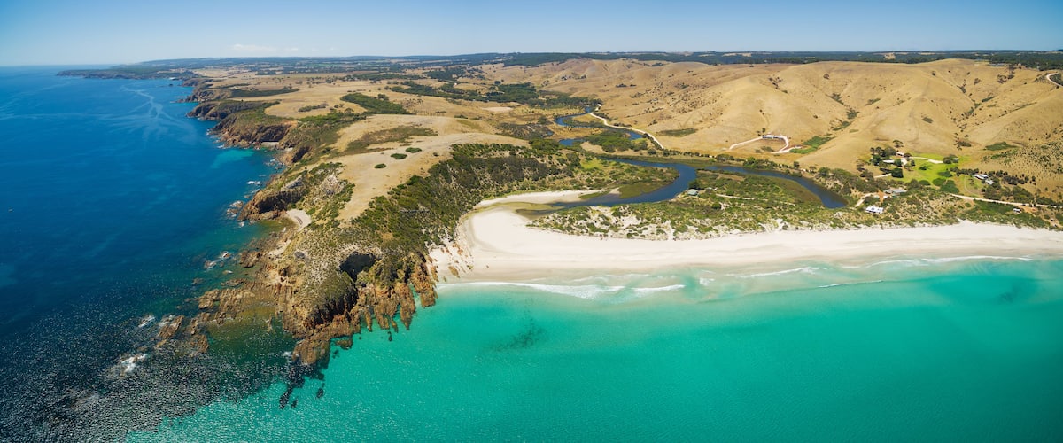 Un paysage côtier caractérisé par une plage de sable, une rivière sinueuse et un terrain vallonné à la végétation clairsemée.