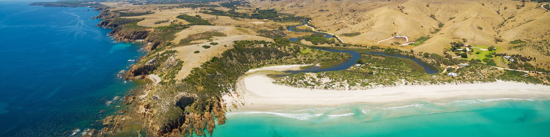 A coastal landscape with a sandy beach, a winding river, and a hilly terrain with sparse vegetation.