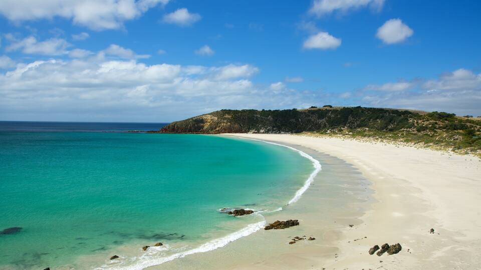 A turquoise beach with white sand and rocky outcrops.