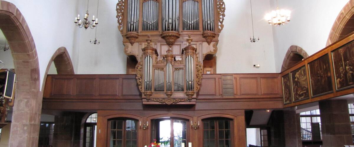 An ornate church interior with a large pipe organ, wooden pews, and a central altar.