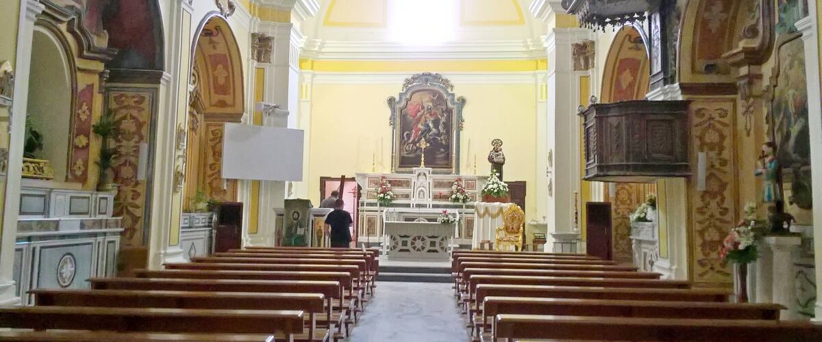 An interior of a church with rows of wooden pews, a central altar, and ornate decorations.