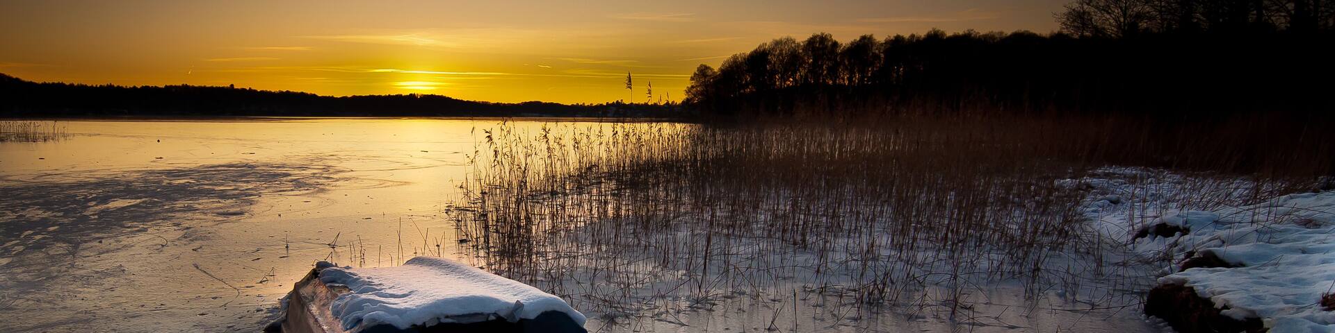 A frozen lake at sunset with a car partially submerged in the ice.