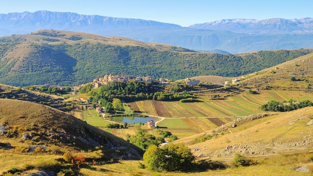Une vallée avec des champs en terrasses, un petit plan d’eau et un ensemble de bâtiments situés sur une colline.