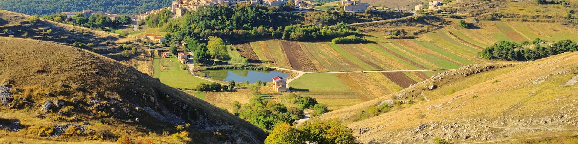 A valley with terraced fields, a small body of water, and a cluster of buildings on a hill.