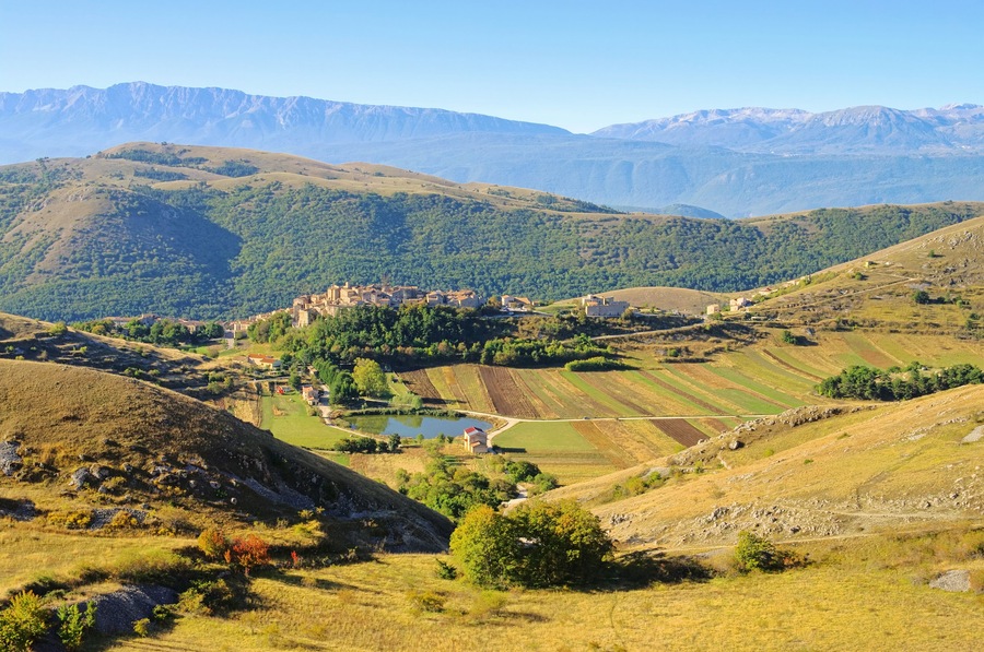 Une vallée avec des champs en terrasses, un petit plan d’eau et un ensemble de bâtiments situés sur une colline.