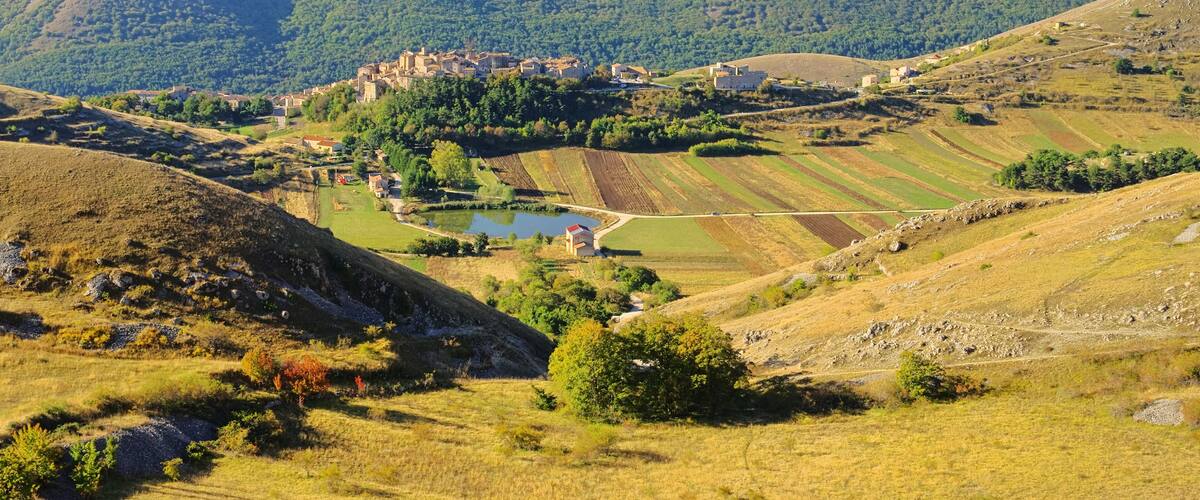 A valley with terraced fields, a small body of water, and a cluster of buildings on a hill.