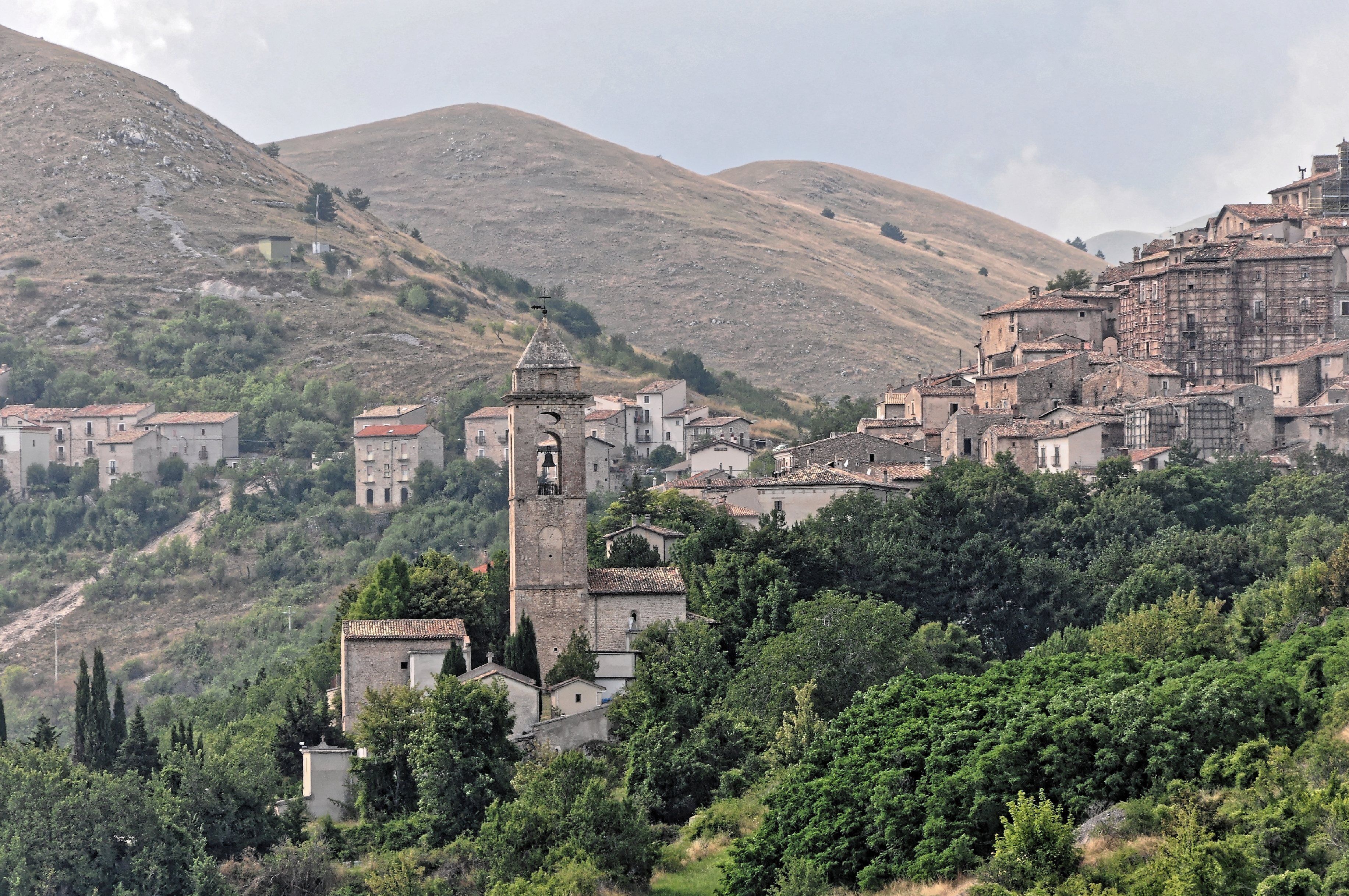 A hillside village with a prominent bell tower, surrounded by lush greenery and traditional buildings.
