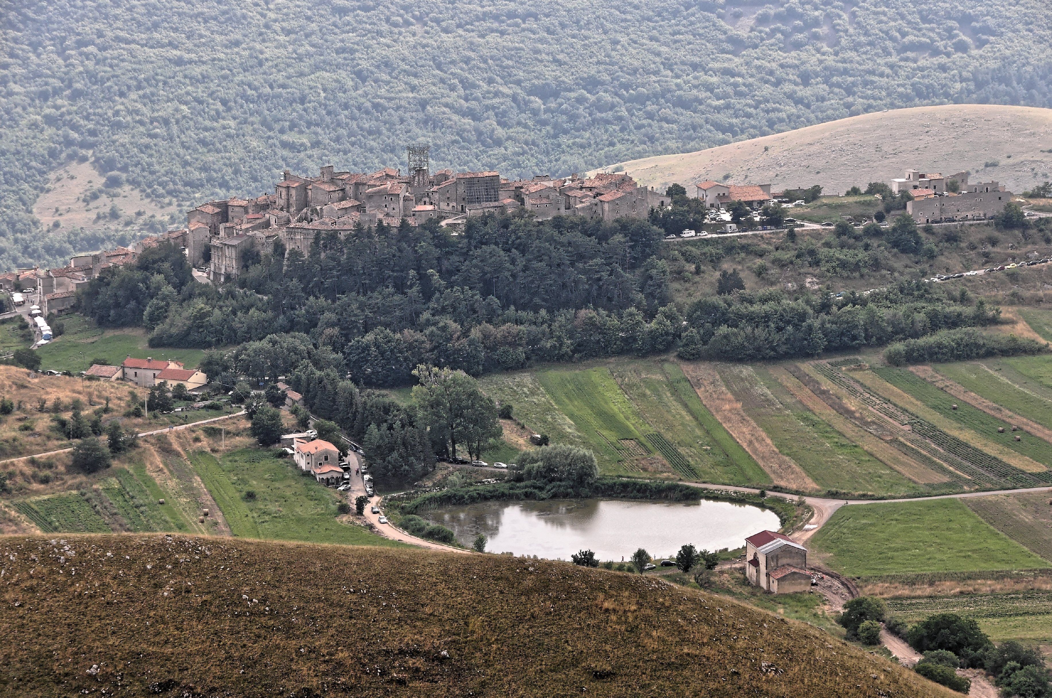 A medieval town nestled in a valley with terraced fields and a lake.
