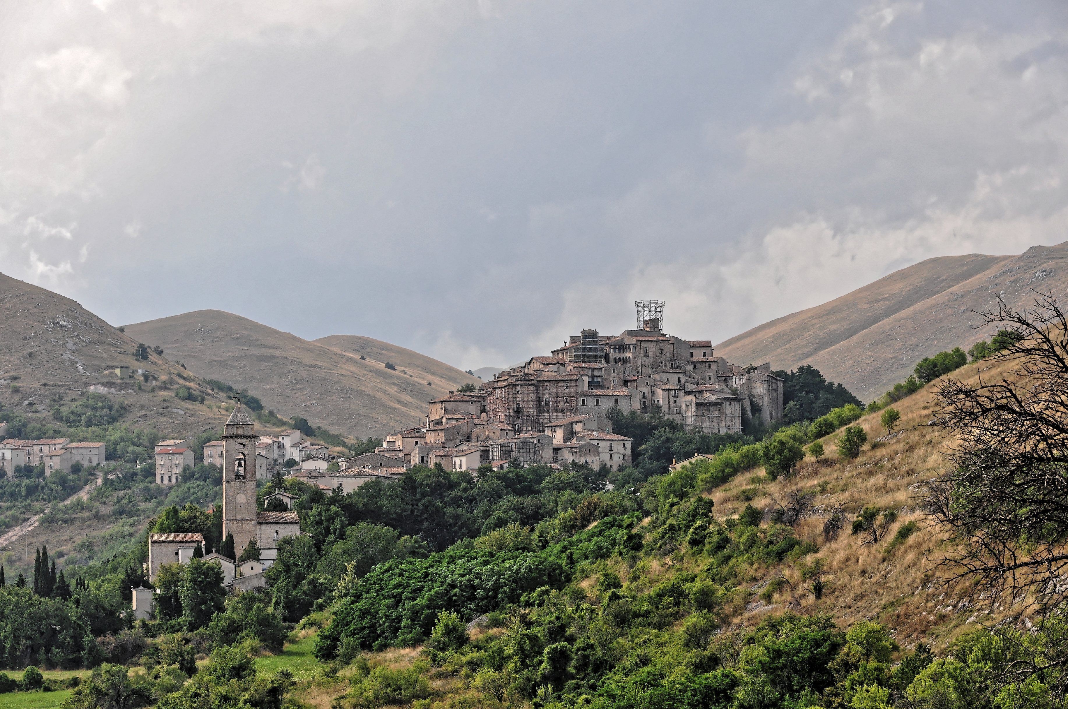 A historic town with a prominent church tower, surrounded by hills and greenery.