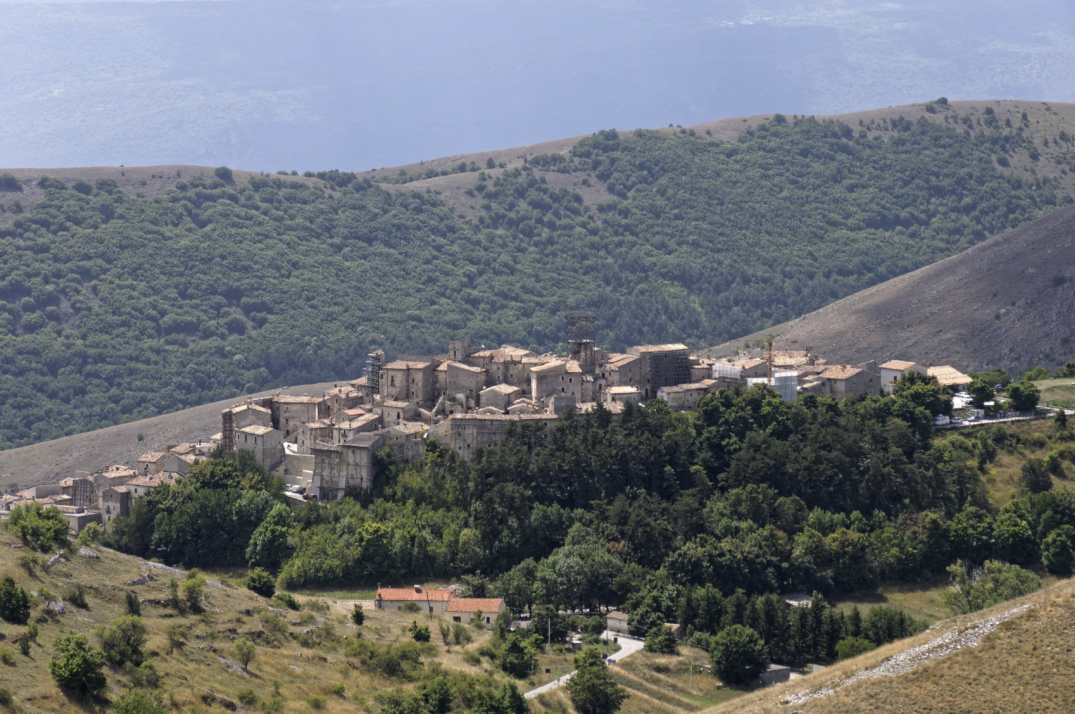 A historic town nestled on a hillside with dense forested areas and a backdrop of rolling hills.